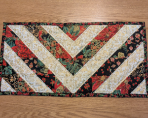 Small table runner with elegant red, green, and black fabric in a chevron pattern.