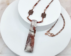 Handmade necklace with jasper pendant, garnet beads, and copper chain on a marble background.