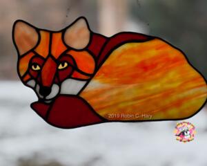 Fox Stained Glass Suncatcher by Robin C. Hary made in shades of red, orange, yellow, cream, and white glass. Hanging in full sunlight.