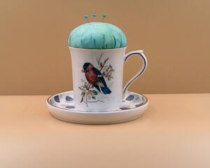 This teacup has a pincushion on the top with some pins and a saucer on the bottom to hold bobbins and other things. It is all one piece.