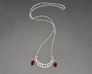 Handmade silver crescent moon phase necklace with red crystal teardrops on chain.