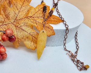 25 inch long handmade necklace with golden quartz leaf pendant, mahogany obsidian beads, and copper chain displayed with fall leaves
