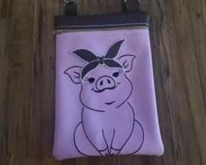 Pink vinyl crossbody bag with embroidered pig design wearing a floral bandana. White zipper top and strap