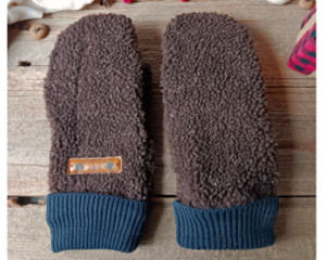 Pair of handmade women’s brown fleece mittens with navy cuffs and leather warmth tag, displayed flat on rustic wood background.