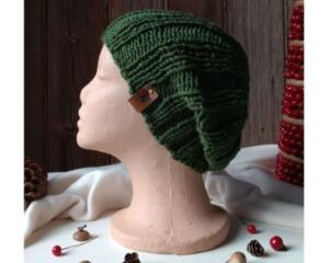 A hand knit green acrylic beanie shown in a slouchy style in a ribbed stitch pattern. For winter holiday gifting for kids ages 6, 7, 8, 9.