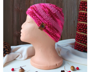 A side view of a handmade baby hat in a pink and red acrylic yarn. Great for winter holiday gifting for newborn babies 0 to 12 months.