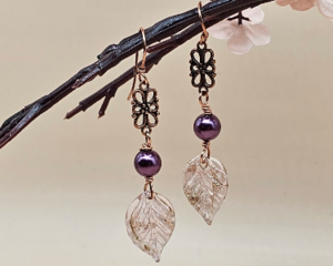 Handmade earrings with lampwork glass leaf charms, plum glass pearls, and copper floral connectors on copper hooks.