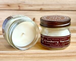 Cranberry and apple scented soy candle in 4oz mason jar. One jar standing up with lid on and one jar on its side with lid off.