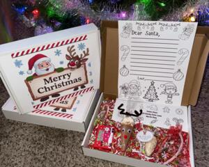 Dear Santa Letter Kit displayed open with letter sheet, candy cane, reindeer cocoa cone, and Christmas gift box under holiday lights