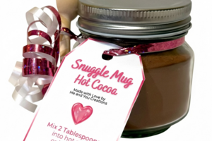 Snuggle Mug handmade hot cocoa jar with reusable glass jar, wooden spoon, pink ribbon, and heart tag on white background