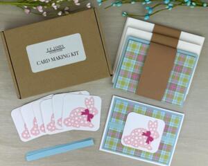 An Easter card making kit with plaid scrapbook paper, pink bunny embellishments, and blue ribbons to make 6 greeting cards.