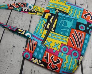 Front view of a multicolor blue geometric African print market tote with a silver front zipper pocket and a silver metal Bass Creations logo.