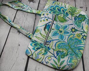 Front view of greens and blues floral pattern market tote with front silver hardware zipper and silver metal Bass Creations logo.