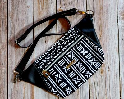 front view of a black and white tribal print waist bag with black faux leather accents, one zippered pocket, and silver hardware with a silver metal Bass Creations logo