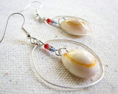 Hand formed, round silver hoop earrings with a dangling cowrie shell and seed bead center accent.