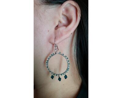 Person models one emerald green and silver wire wrapped dangle earring.