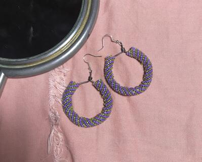 purple and lime green peyote stitch beaded hoop earrings; tube of stitching on a mild steel hoop with silver-plated earring findings. earrings on a pink fabric background.