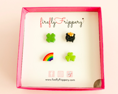 Set of four stud earrings - a four leaf clover, pot of gold, half a rainbow and three leafed shamrock - on a fireflyFrippery branded jewelry card in a hot pink square box