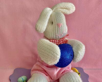 Measurements: Bunny 9" tall  x 4" wide - Plaque 7.5" length x 5" wide. Lilac decorative base with Easter eggs and holding a large royal blue egg.  He is wearing a pink rompler ourt in velour fabric.  Cute collectible or fun centerpiece for the holiday table.