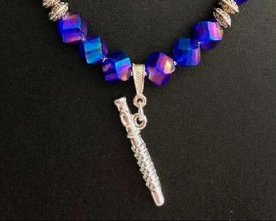 A dainty glass beaded flute necklace in hues purple.  The faceted design of beads leads to the silver 3D flute charm on a small silver bail. This doesn't have to be a dressy necklace.  It is too lovely to leave just for special occasions.  The spaces inbetween  silver-tone purple beads pulls everything together for an outstanding jewelry piece.