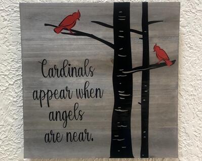 10 inch gray-washed wood sign featuring two black trees trunks and limbs and 2 red cardinals outlined in black, the words Cardinals appear when angels are near appears to the side of the trees in black vinyl