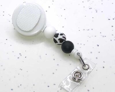 Interchangeable white badge reel with Velcro and white, cow print, and black silicone beads.