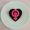 fireflyFrippery hot pink feminist fist on black heart background pin flat lay