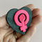fireflyFrippery hot pink feminist fist on black heart background pin in hand
