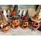 This shows four pumpkin gourds on an entryway table. Each pumpkin has a happy face carved in the shell. Fall hats decorate the pumpkins.