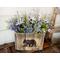This image shows a handmade wood box made from upcycled fencing. A picture of a black bear is wood-burned onto the front. The box holds a faux lavender flower arrangement