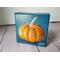 Small square painting of little orange pumpkin with teal blue background.