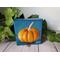 Small square painting of little orange pumpkin with teal blue background.