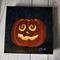 Photo of small square canvas painting of glowing jack o'lantern pumpkin with swirling eyes and a starry sky in the background