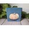 Photo of small square canvas painting of peach colored pumpkin with denim blue colored background