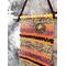 Handmade one-of-a-kind woven wall hanging featuring a charm with a witch flying on a broomstick. 
Colors include golden yellow, orange, terra cotta, dark purple, mauve and black & white tweed woven into a bold horizontal stripe pattern. Measures 3.50 x 14.5 inches including the long 6.5 inch fringe. The hanging thread adds another 3 inches. Woven with cotton, chenille and soft silky bamboo rayon yarn. Top half only.