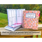 One of the journals shown is sitting on top of another hardcover book in pink, and a blue spiral bound book. A large pink spiral bound book is shown closed to it's right with a label that says Symptom Journal. A note says check out both of our journals Spiral and Hardcover. You are currently viewing the hardcover style.