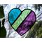 A stained glass heart featuring teal, green, and purple stripes on a nature background