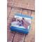 Turquoise blue gift box with gift tag and silver ribbon on neutral wood background. 