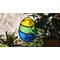 Stained glass Easter Egg suspended over a potted plant ,  additional plants in the background, Egg features yellow, green, and blue stripes