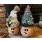 Two Christmas gourds elves are decorating a fireplace hearth. Each elf has a custom hat and a happy face carved out of their gourd shell. 