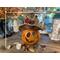 A fall gourd with a happy face carved into the shell. It is 11 inches tall and 5.5 inches wide.  It is part of a fall table display. 