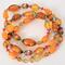 Long orange glass and Lucite beaded necklace with multicolor bead caps and a gold tone clasp.