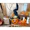 A fall table Halloween table display. There is a pumpkin witch, a vase that holds tree branches, all leaves, and orange berries.