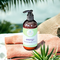 Whole Self Aromatherapy Energy Hand & Body Lotion rests on a beach towel beside lush greenery and a blurred ocean backdrop.