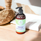 Whole Self Aromatherapy's Energy Hand & Body Lotion rests on a wooden countertop, accompanied by a loofah and spa linens.