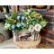 A rustic centerpiece moose box and faux flowers. The arrangement features cedar pine, peonies, blue violets, and gold daisies.