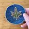 Blue denim patch with fall print fabric hemp leaf with green stitching in the center.