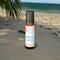 A "Beach Vibes" roll-on wellness blend by Whole Self Aromatherapy on a sandy beach with palm frond and the ocean in the blurred background.