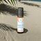 A Beach Vibes roll-on wellness blend by Whole Self Aromatherapy on a sandy beach with palm frond and the ocean in the blurred background.