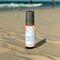 Whole Self Aromatherapy's Beach Vibes roll-on wellness blend on a sandy beach with the ocean and people swimming in the blurred background.